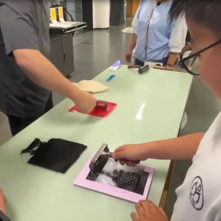 学生在凹版上均匀涂上油墨，使油墨留在版面的凹入线条与图案上。